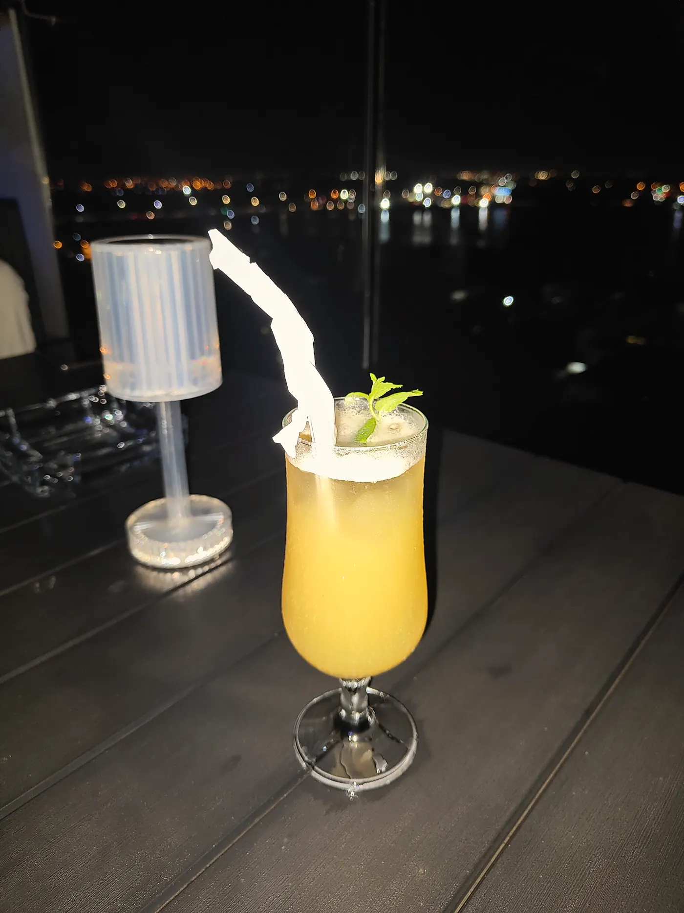 Un cocktail à la mangue sur une table de la terrasse, la lagune de nuit derrière