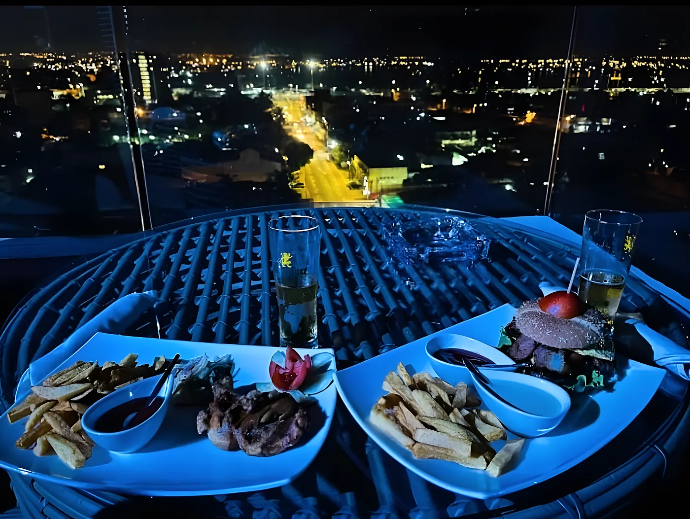 Brochettes et tapas sur une table de la terrasse, la ville illuminée en contrebas