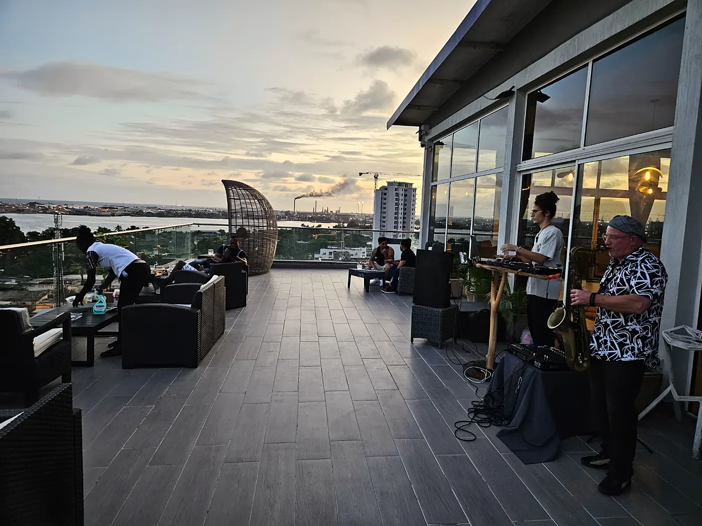 La terrasse au crépuscule, une DJ et un saxophoniste installés près des baies vitrées